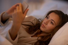 Jovem mulher com o smartphone no quarto da cama em casa imagens de stock Jovem mulher com o smartphone no quarto da cama em casa imagens de stock