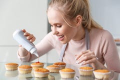jovem mulher de sorriso bonita no avental que prepara queques deliciosos com doce imagens de stock royalty free jovem mulher de sorriso bonita no avental que prepara queques deliciosos com doce imagens de stock royalty free
