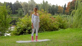 A jovem mulher faz o exercício da ioga que está não em uma esteira do deslizamento em um banco de rio filme A jovem mulher faz o exercício da ioga que está não em uma esteira do deslizamento em um banco de rio filme