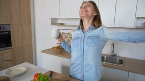 Jovem mulher feliz começar dia novo com o copo do chá nas mãos, estando no meio da cozinha na mesa de cozinha na manhã filme Jovem mulher feliz começar dia novo com o copo do chá nas mãos, estando no meio da cozinha na mesa de cozinha na manhã filme