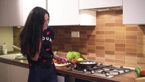 A jovem mulher feliz em um bom humor nos pijamas está falando no telefone e está cozinhando um café da manhã em casa Ela stewes a video estoque A jovem mulher feliz em um bom humor nos pijamas está falando no telefone e está cozinhando um café da manhã em casa Ela stewes a video estoque
