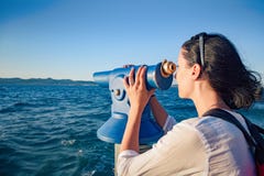 A jovem mulher olha em um telescópio ou em binóculos pelo mar fotos de stock royalty free A jovem mulher olha em um telescópio ou em binóculos pelo mar fotos de stock royalty free