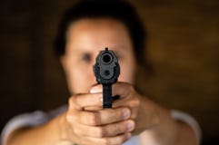 Jovem mulher que guarda uma arma e apontar fotografia de stock royalty free Jovem mulher que guarda uma arma e apontar fotografia de stock royalty free