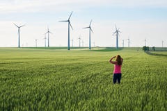 Jovem mulher que olha para turbinas eólicas no nascer do sol, em um campo do trigo verde Conceito para soluções sustentáveis da e imagens de stock Jovem mulher que olha para turbinas eólicas no nascer do sol, em um campo do trigo verde Conceito para soluções sustentáveis da e imagens de stock