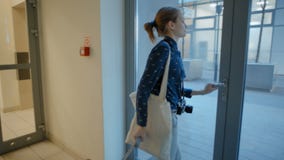 Jovem senhora Leaving Elevator e construção à rua com mala de viagem, saco e câmera video estoque Jovem senhora Leaving Elevator e construção à rua com mala de viagem, saco e câmera video estoque
