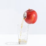 Jugo que fluye de una manzana madura en un vidrio Concepto creativo de jugo fresco fotos de archivo libres de regalías Jugo que fluye de una manzana madura en un vidrio Concepto creativo de jugo fresco fotos de archivo libres de regalías