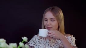Junge Blondine auf einem schwarzen Hintergrund Sie trinkt ihren Kaffee und schaut träumerisch stock footage Junge Blondine auf einem schwarzen Hintergrund Sie trinkt ihren Kaffee und schaut träumerisch stock footage