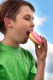 Junge, der einen leckeren rosa gefrorenen Donut (Donut, beißt) stockbilder Junge, der einen leckeren rosa gefrorenen Donut (Donut, beißt) stockbilder