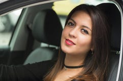 Junge Frau der Nahaufnahme, die im Auto lächelt zur Kamera sitzt, wie vom äußeren Treiberfenster gesehen, weibliches Fahrerkonzep lizenzfreie stockbilder Junge Frau der Nahaufnahme, die im Auto lächelt zur Kamera sitzt, wie vom äußeren Treiberfenster gesehen, weibliches Fahrerkonzep lizenzfreie stockbilder