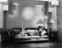 Junge Frau, die auf einer Couch liegt und eine Zeitschrift liest (alle dargestellten Personen sind nicht längeres lebendes und ke stockfoto Junge Frau, die auf einer Couch liegt und eine Zeitschrift liest (alle dargestellten Personen sind nicht längeres lebendes und ke stockfoto