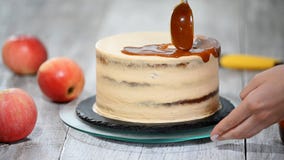 Junge Frau, die bei Tisch Karamellsoße auf köstlichen selbst gemachten Kuchen aufträgt Köstlicher Kuchen mit Apfel und Schlagsahn stock video footage Junge Frau, die bei Tisch Karamellsoße auf köstlichen selbst gemachten Kuchen aufträgt Köstlicher Kuchen mit Apfel und Schlagsahn stock video footage