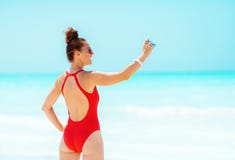 Junge Frau, die Fotos mit Retro- Fotokamera auf Seeküste macht lizenzfreie stockfotos Junge Frau, die Fotos mit Retro- Fotokamera auf Seeküste macht lizenzfreie stockfotos
