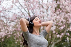 Junge Frau, die Musik auf drahtlosen Kopfh?rern in einem Park mit Kirschbl?tenb?umen h?rt lizenzfreie stockfotos Junge Frau, die Musik auf drahtlosen Kopfh?rern in einem Park mit Kirschbl?tenb?umen h?rt lizenzfreie stockfotos
