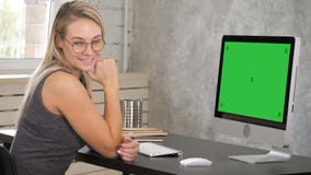 Junge Frau, die zur Kamera sitzt auf ihrem Arbeitsplatz lächelt Grüne Schirm-Modell-Anzeige stock video Junge Frau, die zur Kamera sitzt auf ihrem Arbeitsplatz lächelt Grüne Schirm-Modell-Anzeige stock video