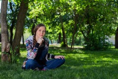 Junge Frau im Denimoverall, der auf dem grünen Gras im Park sitzt stockfotografie Junge Frau im Denimoverall, der auf dem grünen Gras im Park sitzt stockfotografie