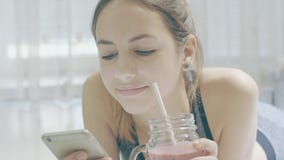 Junge Frau ist das Trinken Smoothies und Anwendung einer Eignungs-APP auf ihrem Smartphone Junge Frau ist das Trinken Smoothies und Anwendung einer Eignungs-APP auf ihrem Smartphone