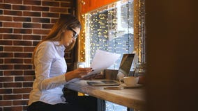junge Geschäftsfrau, die in einem Café sitzt und Dokumente studiert stock video footage junge Geschäftsfrau, die in einem Café sitzt und Dokumente studiert stock video footage