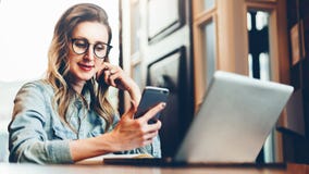 Junge Geschäftsfrau sitzt in der Kaffeestube bei Tisch vor Computer und Notizbuch, unter Verwendung des Smartphone Ein Bündel Leu lizenzfreies stockbild Junge Geschäftsfrau sitzt in der Kaffeestube bei Tisch vor Computer und Notizbuch, unter Verwendung des Smartphone Ein Bündel Leu lizenzfreies stockbild