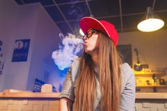 Junge hübsche Frau im roten Kappenrauche eine elektronische Zigarette am vape Shop lizenzfreie stockfotografie Junge hübsche Frau im roten Kappenrauche eine elektronische Zigarette am vape Shop lizenzfreie stockfotografie