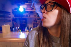 Junge hübsche Frau im roten Kappenrauche eine elektronische Zigarette am vape Shop nahaufnahme lizenzfreies stockbild Junge hübsche Frau im roten Kappenrauche eine elektronische Zigarette am vape Shop nahaufnahme lizenzfreies stockbild