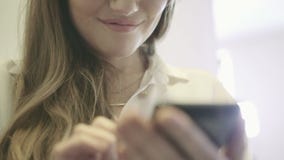 Junge lächelnde Frau, die in der Hand einen Smartphone hält und in Internet surft