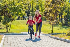 Junge Mutter, die ihrem Sohn beibringt, wie man Fahrrad im Park fährt lizenzfreie stockfotos Junge Mutter, die ihrem Sohn beibringt, wie man Fahrrad im Park fährt lizenzfreie stockfotos