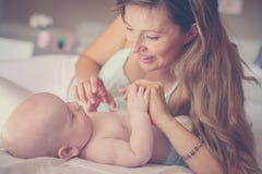 Junge Mutter, die mit ihrem Baby im Bett spielt Mutter, die i genießt Lizenzfreie Stockfotografie Junge Mutter, die mit ihrem Baby im Bett spielt Mutter, die i genießt Lizenzfreie Stockfotografie