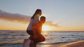 Junge Paare in der Liebe, die Spaß auf dem Strand an Sonnenuntergang berugi hat Ein Mädchen sitzt auf den Schultern von den Männe stock footage Junge Paare in der Liebe, die Spaß auf dem Strand an Sonnenuntergang berugi hat Ein Mädchen sitzt auf den Schultern von den Männe stock footage