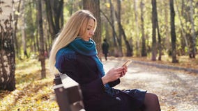 Junge sch?ne blonde Frau, die auf Bank und Gebrauch Smartphone im herbstlichen Park sitzt 3840x2160, 4K stock footage Junge sch?ne blonde Frau, die auf Bank und Gebrauch Smartphone im herbstlichen Park sitzt 3840x2160, 4K stock footage