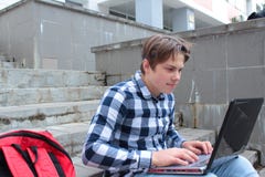 Jungenjugendlichschüler oder -student sitzt auf der Treppe und arbeitet im Computer, tragende Gläser, in einem Hemd und lächelt, stockbild Jungenjugendlichschüler oder -student sitzt auf der Treppe und arbeitet im Computer, tragende Gläser, in einem Hemd und lächelt, stockbild