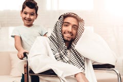 Junger arabischer Mann auf Rollstuhl mit lächelndem Sohn lizenzfreie stockfotografie Junger arabischer Mann auf Rollstuhl mit lächelndem Sohn lizenzfreie stockfotografie