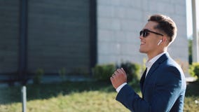 Junger Geschäftsmann mit Sonnenbrille draußen hörend Musik auf seinem Smartphone und dem Tanzen Er gehend nahe Büro stock footage Junger Geschäftsmann mit Sonnenbrille draußen hörend Musik auf seinem Smartphone und dem Tanzen Er gehend nahe Büro stock footage