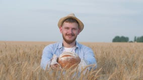 Junger glücklicher Getreidebauer, gut aussehender Mann im Strohhut gibt Sie am geschmackvollen gebackenen Brot und am Lächeln der stock footage Junger glücklicher Getreidebauer, gut aussehender Mann im Strohhut gibt Sie am geschmackvollen gebackenen Brot und am Lächeln der stock footage