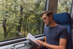 Junger gut aussehender Mann, der ein Buch beim Reisen mit dem Zug liest lizenzfreie stockbilder Junger gut aussehender Mann, der ein Buch beim Reisen mit dem Zug liest lizenzfreie stockbilder