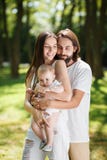 Junger hübscher brunette Mann umarmt leicht seine schöne Frau und kleine Tochter im Park an einem sonnigen Tag stockfoto Junger hübscher brunette Mann umarmt leicht seine schöne Frau und kleine Tochter im Park an einem sonnigen Tag stockfoto