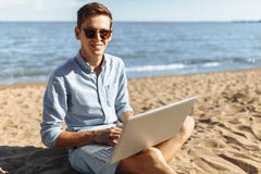 Junger Kerl mit den Gläsern, arbeitend an seinem Laptop auf dem Strand, arbeiten im Urlaub, passend für die Werbung, Texteinfügun stockbild Junger Kerl mit den Gläsern, arbeitend an seinem Laptop auf dem Strand, arbeiten im Urlaub, passend für die Werbung, Texteinfügun stockbild