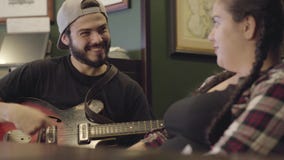 Junger lächelnder bärtiger Mann, der Gitarre in der Stange, attraktive pralle Frau sitzt nahe dem Gesang spielt Freizeit an der K stock footage Junger lächelnder bärtiger Mann, der Gitarre in der Stange, attraktive pralle Frau sitzt nahe dem Gesang spielt Freizeit an der K stock footage