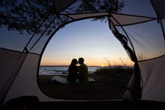 Junger Paarmann und -frau, die Rest am touristischen Zelt und an brennendem Lagerfeuer auf Seeufer nahe Wald hat stockfotografie Junger Paarmann und -frau, die Rest am touristischen Zelt und an brennendem Lagerfeuer auf Seeufer nahe Wald hat stockfotografie
