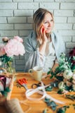 Junger weiblicher Florist, der am Telefon spricht und Anmerkungen am Blumenladen macht lizenzfreie stockbilder Junger weiblicher Florist, der am Telefon spricht und Anmerkungen am Blumenladen macht lizenzfreie stockbilder