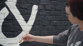 Junger weiblicher Maler kreativer Maler Rear-Ansicht, der weißes Design auf der schwarzen Backsteinmauer in der Kaffeestube macht stock video footage Junger weiblicher Maler kreativer Maler Rear-Ansicht, der weißes Design auf der schwarzen Backsteinmauer in der Kaffeestube macht stock video footage