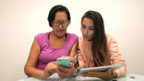 Junges Mischrassemädchen, das ihrer älteren asiatischen Mutter etwas verwendet Handy zeigt 4K stock video Junges Mischrassemädchen, das ihrer älteren asiatischen Mutter etwas verwendet Handy zeigt 4K stock video