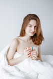 Kaukasische meisjesvrouw met lange rode haarzitting in verpakt die bed met deken, holdingskop wordt behandeld stock foto Kaukasische meisjesvrouw met lange rode haarzitting in verpakt die bed met deken, holdingskop wordt behandeld stock foto