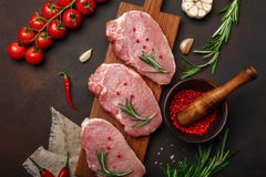 Kawałki surowy wieprzowina stek na tnącej desce z czereśniowych pomidorów, rozmarynów, czosnku, pieprzu, soli i pikantności moźdz zdjęcie stock Kawałki surowy wieprzowina stek na tnącej desce z czereśniowych pomidorów, rozmarynów, czosnku, pieprzu, soli i pikantności moźdz zdjęcie stock