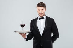 Kellner im Smoking, das Glas Rotwein auf Behälter hält lizenzfreie stockfotografie Kellner im Smoking, das Glas Rotwein auf Behälter hält lizenzfreie stockfotografie