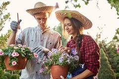 Kerl- und Mädchengärtner in den Töpfen eines Strohhutgriffs mit wunderbarer Petunie auf dem Gartenweg herein an einem sonnigen Ta lizenzfreies stockbild Kerl- und Mädchengärtner in den Töpfen eines Strohhutgriffs mit wunderbarer Petunie auf dem Gartenweg herein an einem sonnigen Ta lizenzfreies stockbild