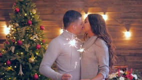 Kerstmisfamilie, jonge het houden van paartribune dicht bij elkaar met de lichten van Bengalen op achtergrond van een Kerstboom stock videobeelden Kerstmisfamilie, jonge het houden van paartribune dicht bij elkaar met de lichten van Bengalen op achtergrond van een Kerstboom stock videobeelden
