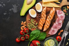 Keto-lunch eller matställe - grillad lax, grönsaker, kokt ägg, vatten med limefrukt, muttrar, skinka och ost på en mörk bakgrund arkivbild Keto-lunch eller matställe - grillad lax, grönsaker, kokt ägg, vatten med limefrukt, muttrar, skinka och ost på en mörk bakgrund arkivbild