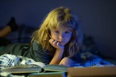 Kid reading bedtime story in dark room. Child reading book. Little boy read books in living room watching pictures in