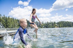 Kids jumping off the dock into a beautiful mountain lake. Having fun on a summer vacation stock photo Kids jumping off the dock into a beautiful mountain lake. Having fun on a summer vacation stock photo