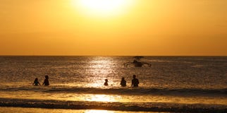 Kids playing at the beach with fisherman boat in Bali, Indonesia during sunset at the beach. stock photo Kids playing at the beach with fisherman boat in Bali, Indonesia during sunset at the beach. stock photo